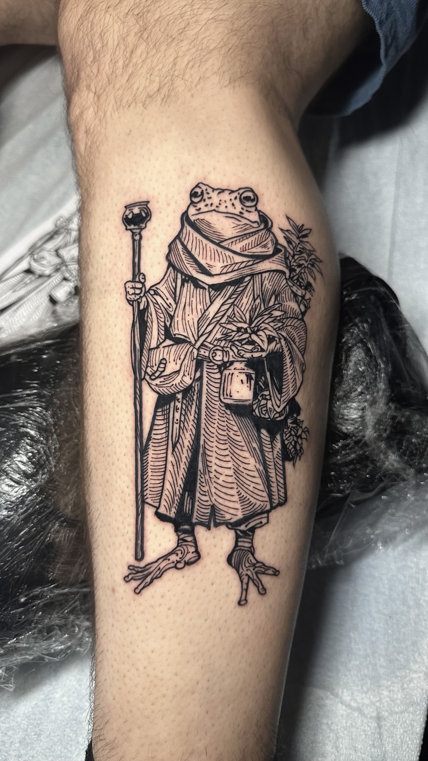 Arsen’s engraving style tattoo of a traveling frog in a robe, carrying a staff and satchel